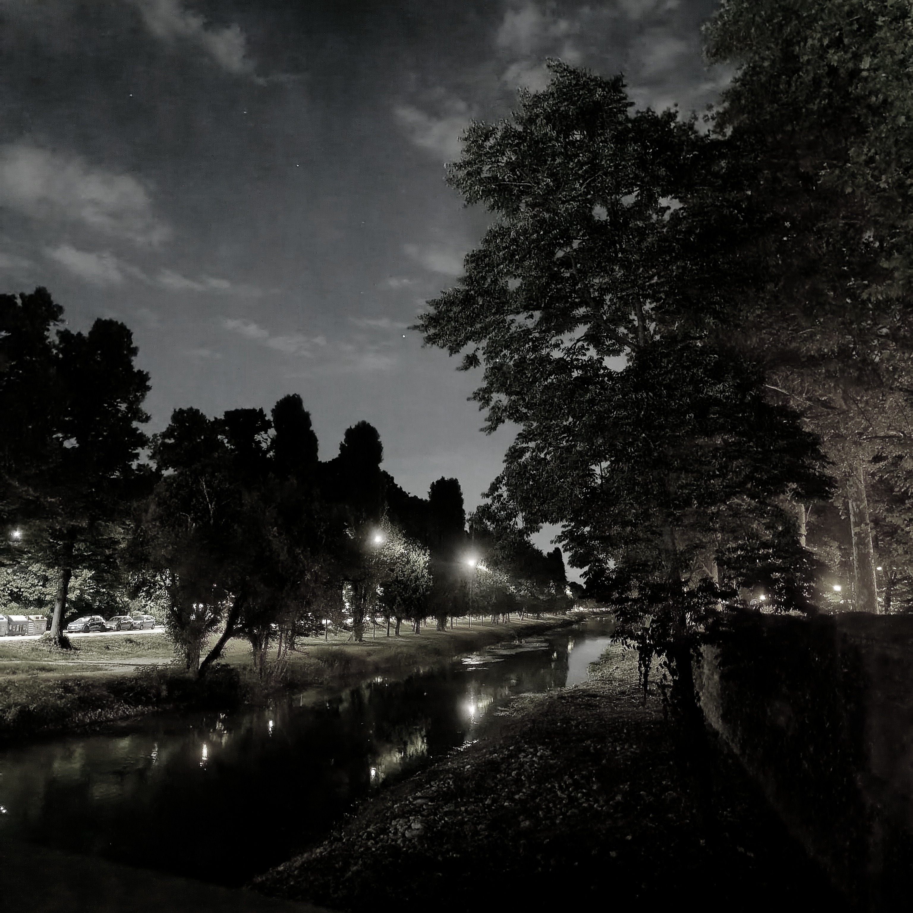 Un canale navigabile, costeggiato da alberi, all'imbrunire. Alcuni lampioni si riflettono sull'acqua