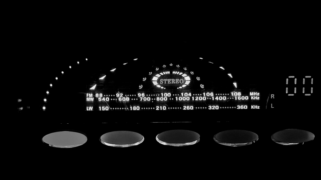 A black-and-white view of an illuminated digital radio tuner display against a dark background, with five round buttons aligned along the bottom. The center features a glowing "STEREO" indicator framed by an arched meter, positioned above three horizontal frequency bands labeled "FM 88 ... 92 ... 96 ... 100 ... 104 ... 106 ... 108 MHz", "MW 540 ... 600 ... 700 ... 800 ... 1000 1200 ... 1400 ... 1600 KHz", and "LW 150 ... 180 ... 210 ... 260 ... 320 ... 360 KHz". To the right, glowing text shows "R" and "L" channel indicators alongside a digital display reading "00".